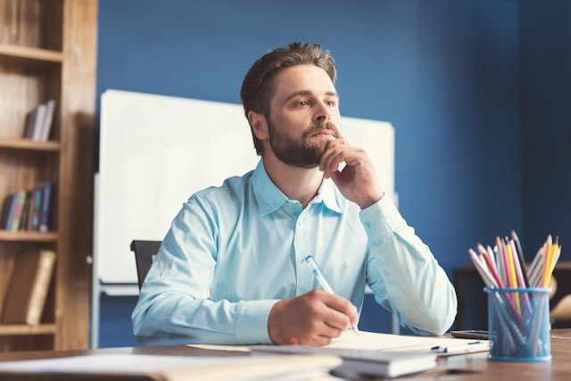 young-man-with-beard-sitting-at-table-with-pen